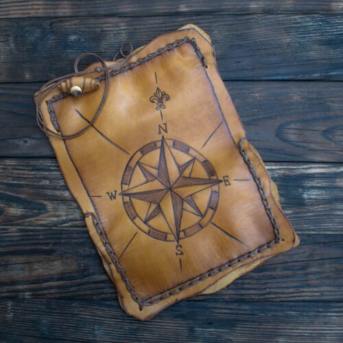 Handcrafted Leather Tobacco Case with Compass Pyrography This is an exceptional, handcrafted leather tobacco case, designed with a rustic, nautical, or adventurous aesthetic. Materials and Texture Material: The case is made from genuine, thick leather, which has been dyed a warm, rich light-tan or natural caramel color. Feel: The leather has a smooth, yet substantial and slightly stiff feel, suggesting durability. It is not rigid like wood, but holds its shape well. You can feel the natural, irregular edges of the hide, giving it an organic, rustic character. Stitching: The outer edges of the case are secured with a thick, braided leather cord (like a whipstitch) that creates a raised, tactile border all the way around. Design and Pyrography (The Tactile Art) The most striking feature is a large, central design created by pyrography (the art of burning/etching a design into the leather). This burning process creates a smooth, shallow indentation and a noticeable change in texture, making the design fully tactile. The Compass Rose: The central image is a detailed compass rose, a traditional navigational symbol. You can feel the distinct points and lines radiating from the center. The primary directional points are clearly marked with the capital letters N (North), S (South), E (East), and W (West). The letters are etched in a bold, simple font. Fleur-de-lis: Just above the 